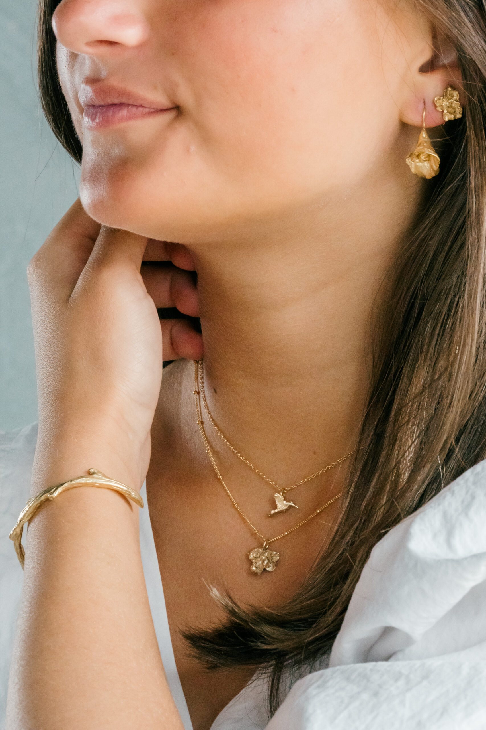 A woman wearing dainty gold necklaces, bracelets, and earrings.
