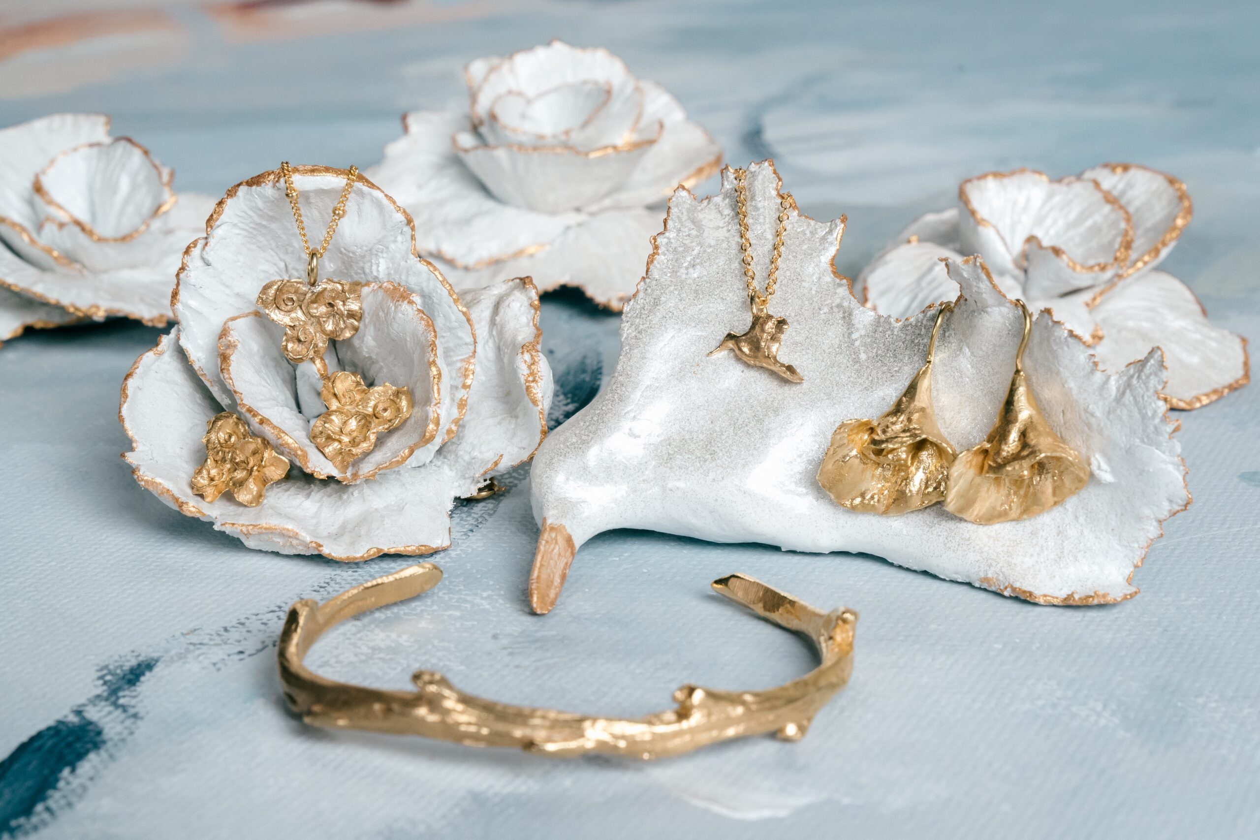 Gold jewelry pieces displayed on oyster shells from Mary Frances Maker, designed by Charissa Owens Art.
