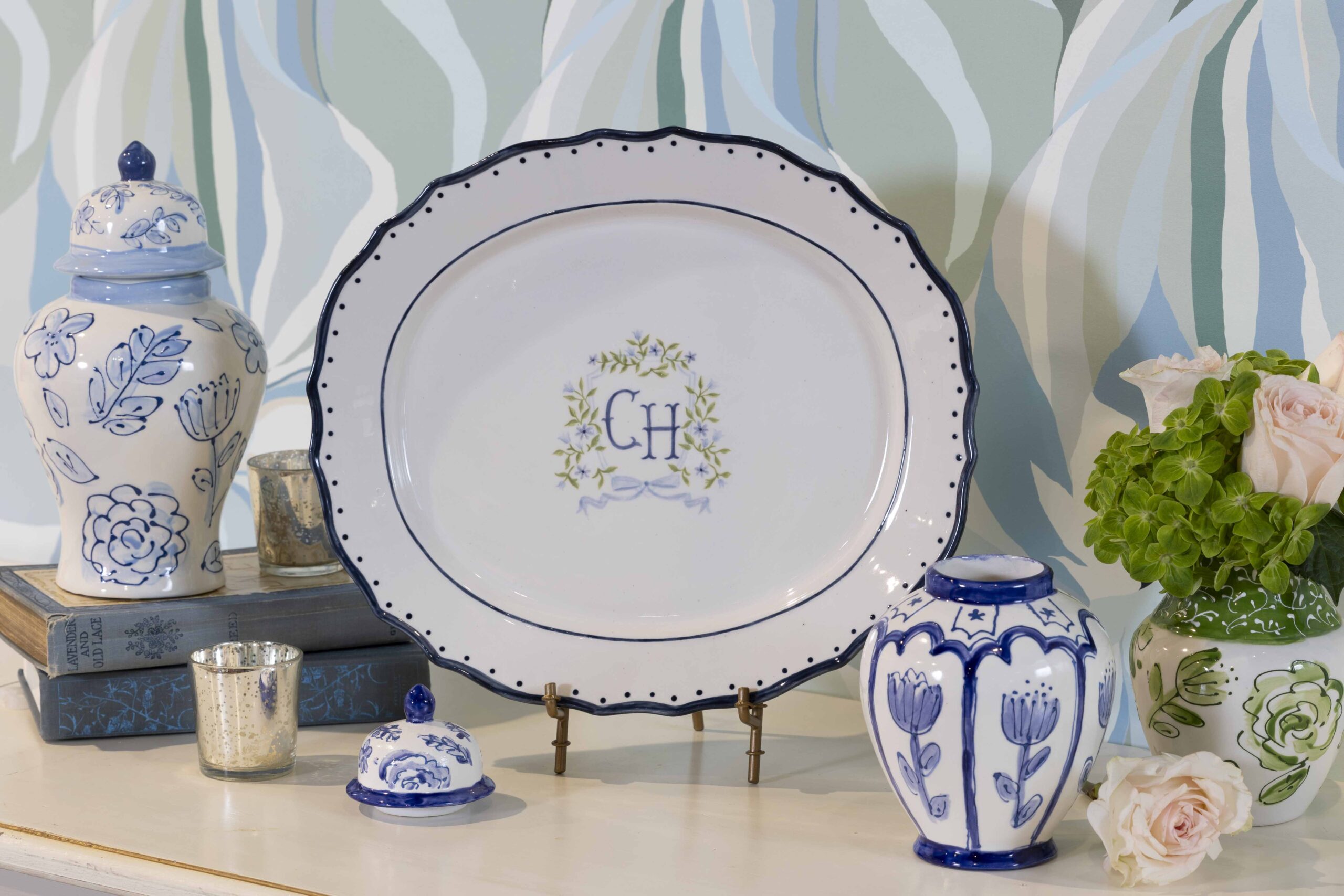 A platter with scalloped edges and a monogram on it, near blue and white ginger jars and vases.