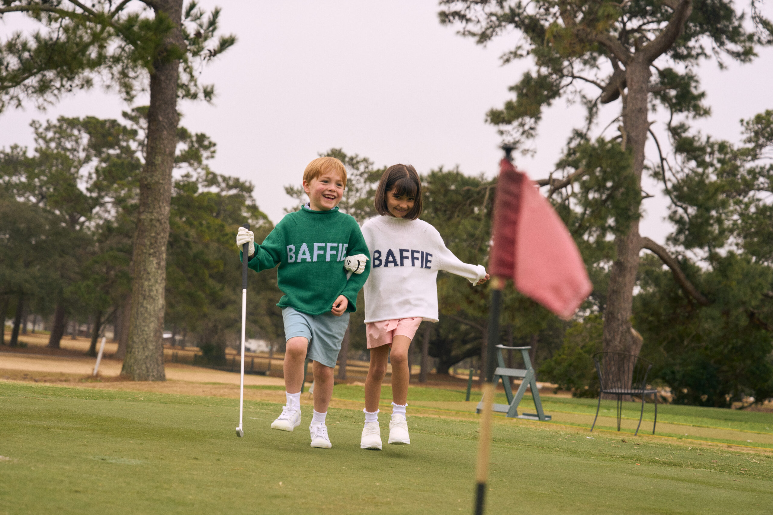 A boy and girl on a golf course in Baffie sweaters