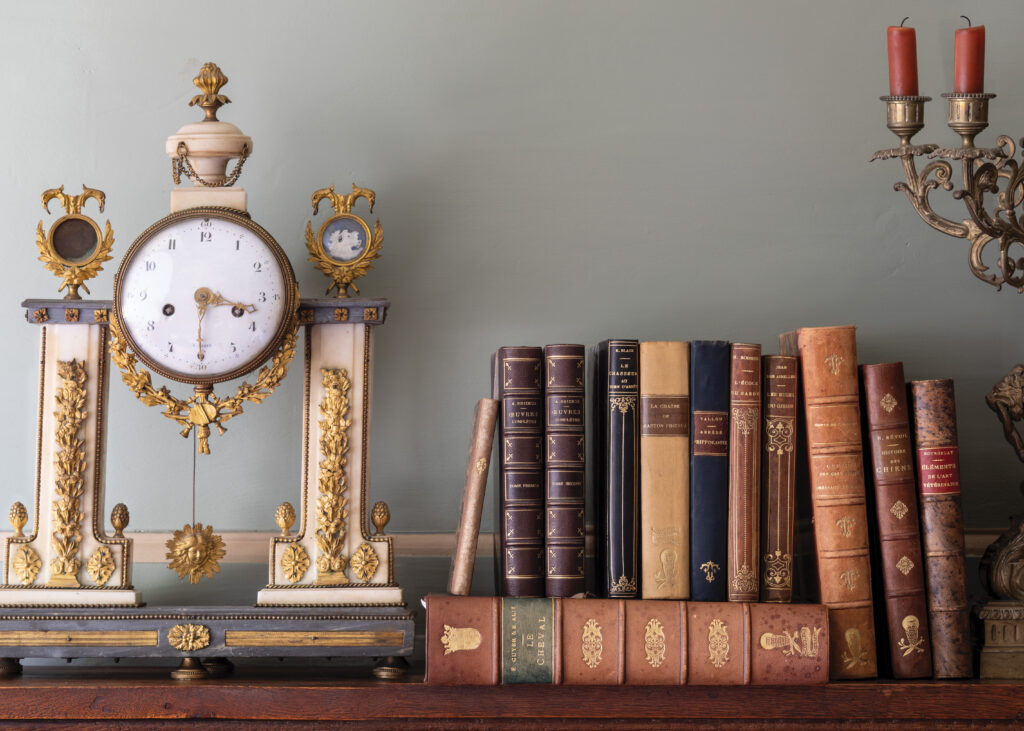 Antique clock next to stacked books and a candelabra