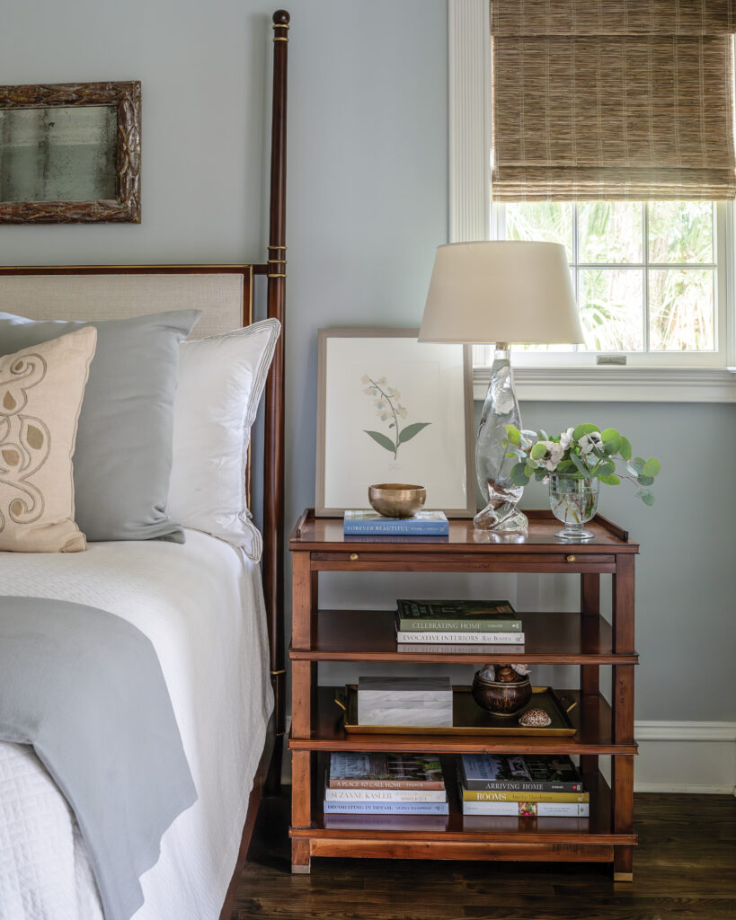 Bedside table with shelves of stacked books and flower print next to white and blue bed 