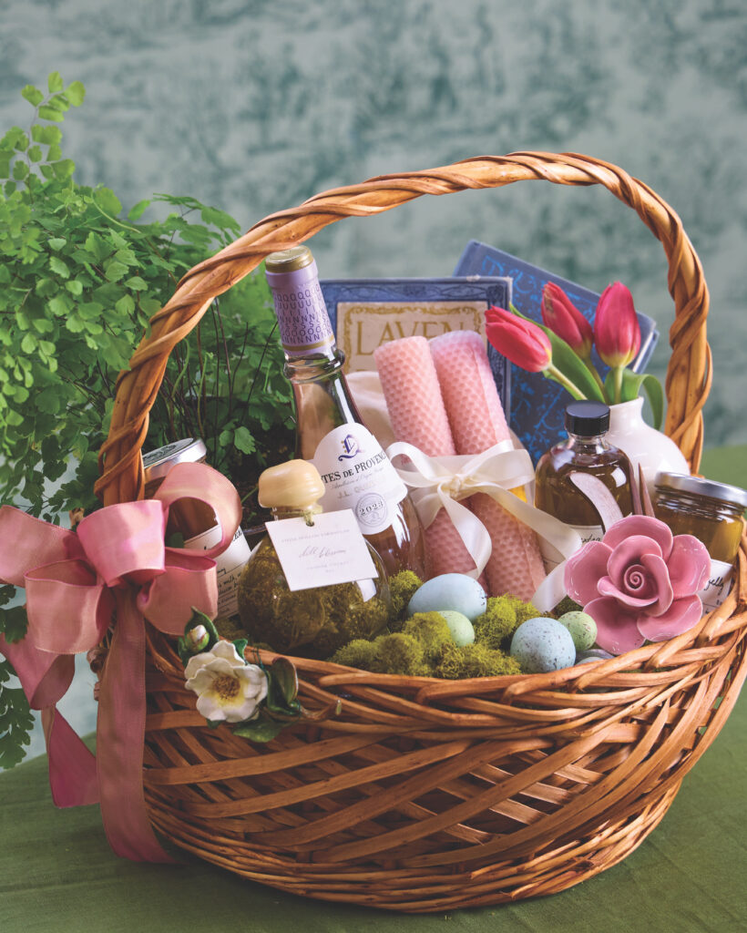 An Easter basket filled with a bottle of wine, candlesticks, tulips, a book, and easter eggs.