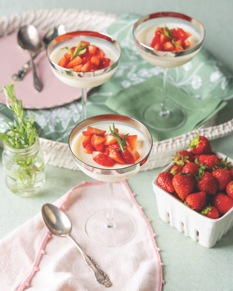 Three coupe glasses filled with panna cotta and topped with sliced strawberries.