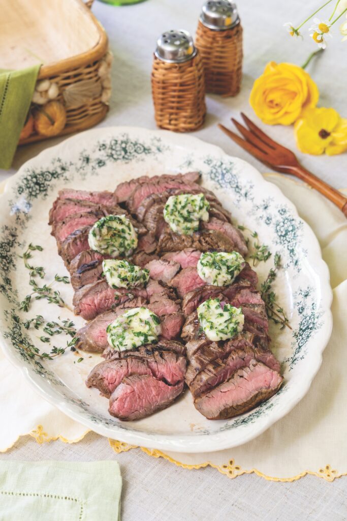 Slices of steak on a blue and white platter topped with garlic herb butter.