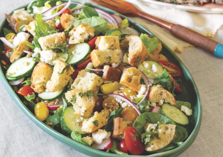 Panzanella salad in an oval serving dish with a platter of steak in the background.
