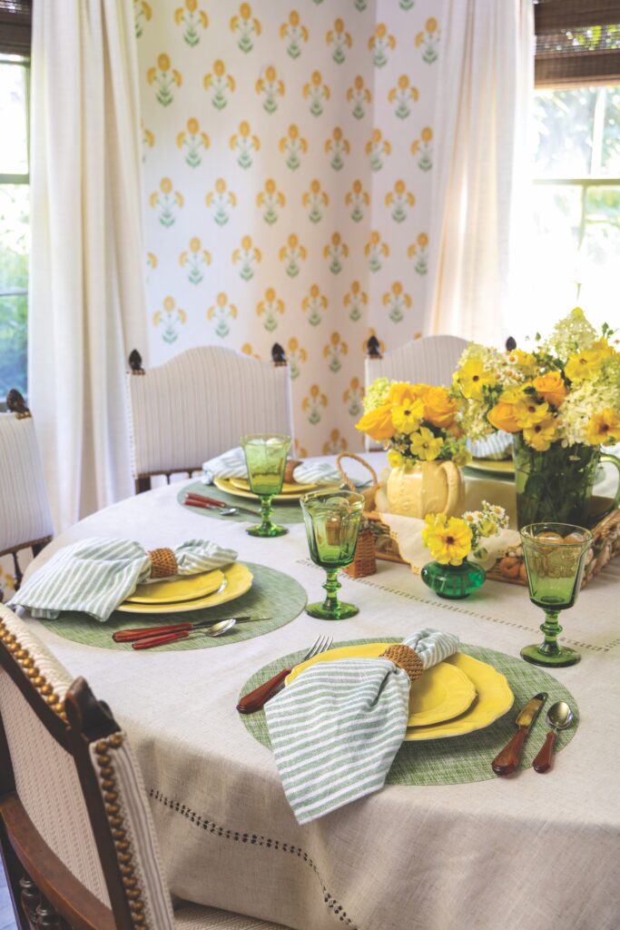 A circle table with several place settings with a couple of yellow floral arrangements in the center.