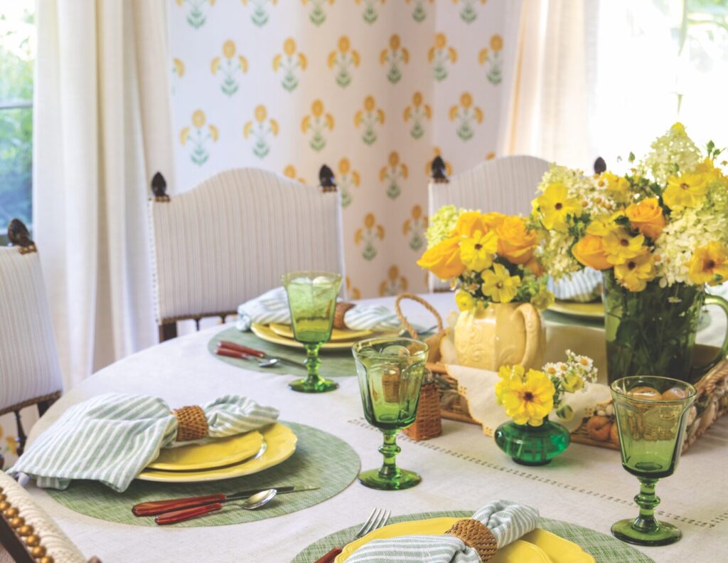 A circle table with several place settings with a couple of yellow floral arrangements in the center.
