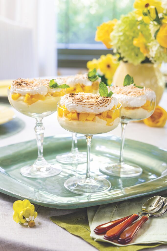 Mini mango cheesecake trifles in coupe glasses, served on a green tray.