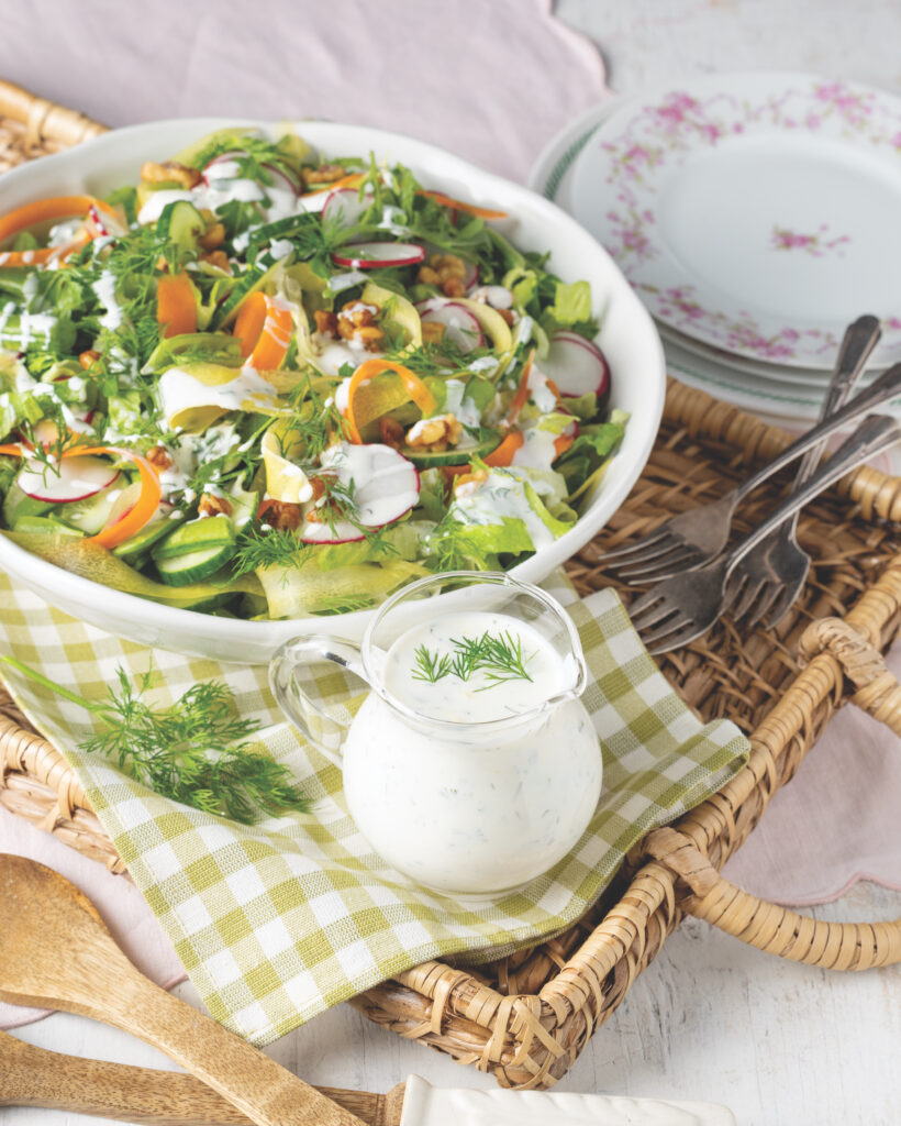 A woven tray holding a small pitcher of ranch and a white bowl with salad.