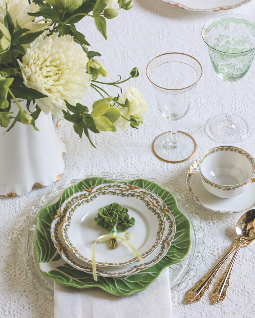 An all-white place setting, with a cabbage ware dinner plate, a white pitcher of flowers, and a bundle of clovers atop the white bread plate.