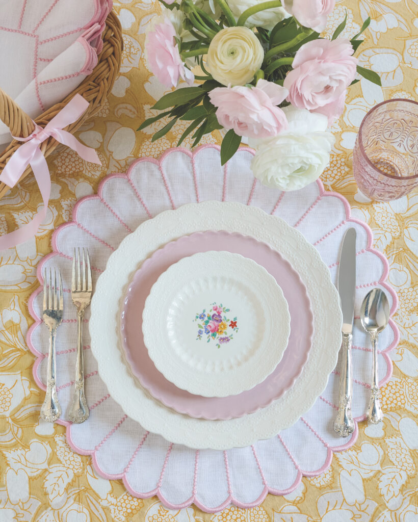 A yellow tablecloth, with a white-and-pink scalloped placemat and white and pink dishes atop it.