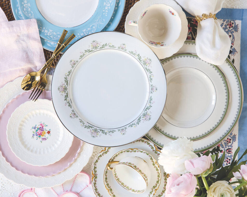 Several stacks of plates displayed from over head, with a set of gold flatware, a teacup, and some flowers.