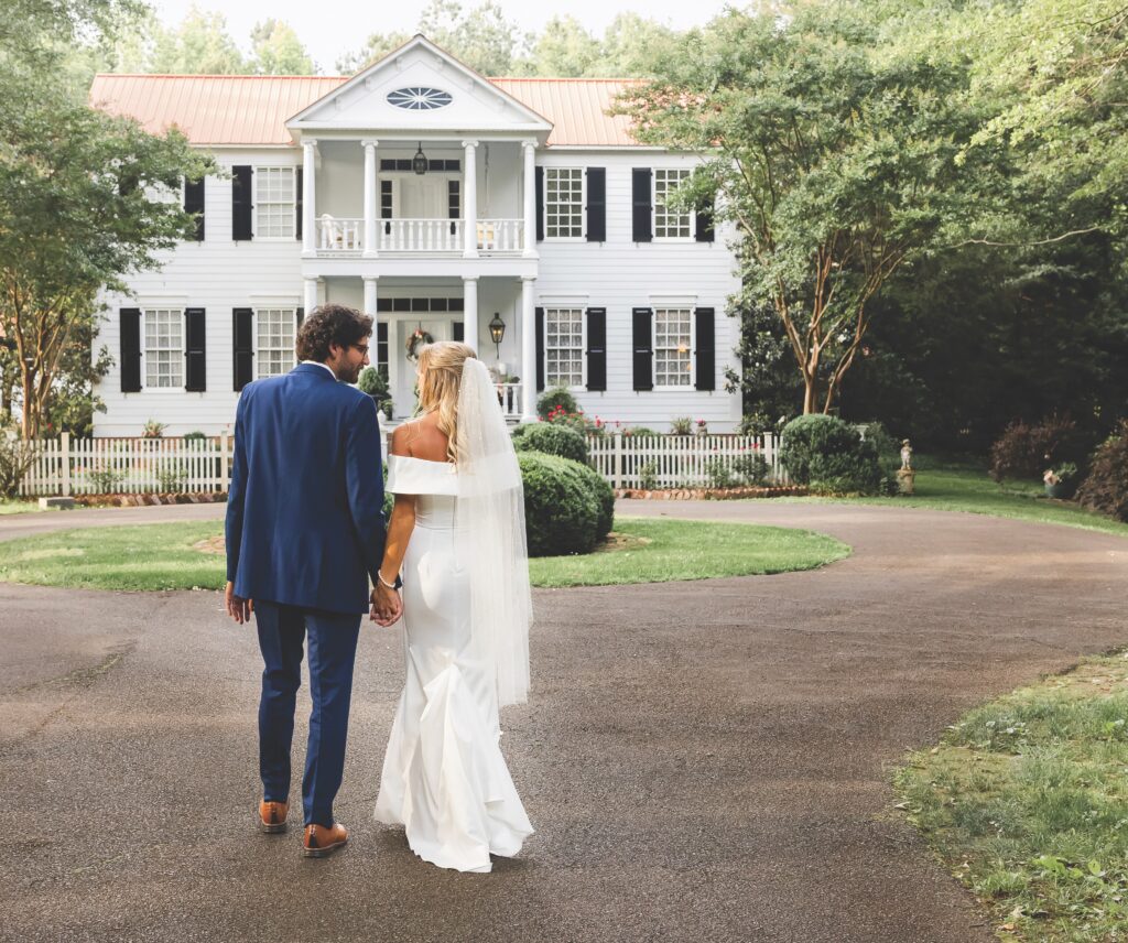 A newlywed couple walking toward a white house.