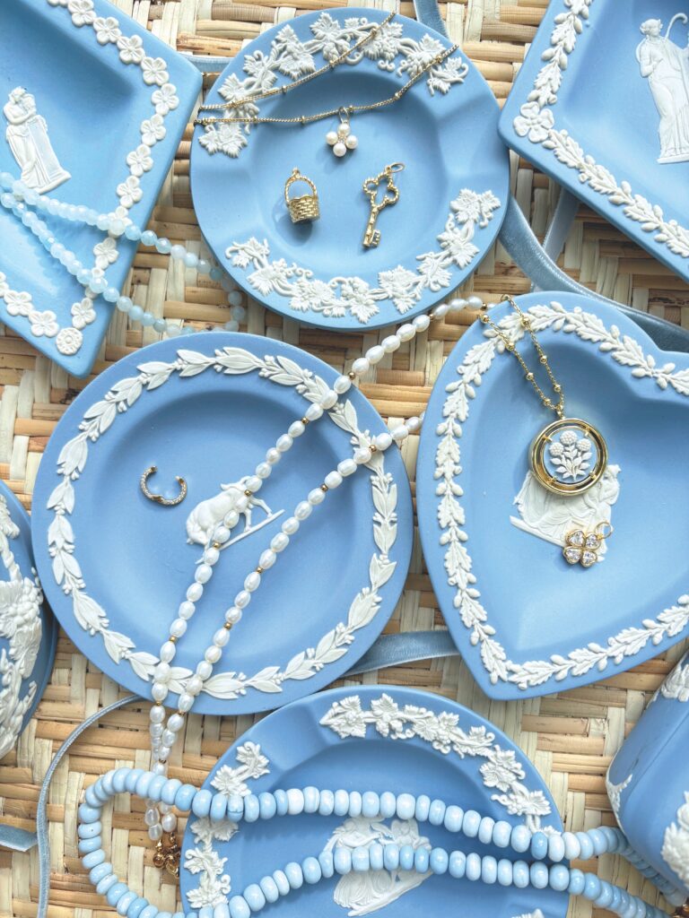 Several Wedgwood blue jewelry dishes holding beaded necklaces and pendants.