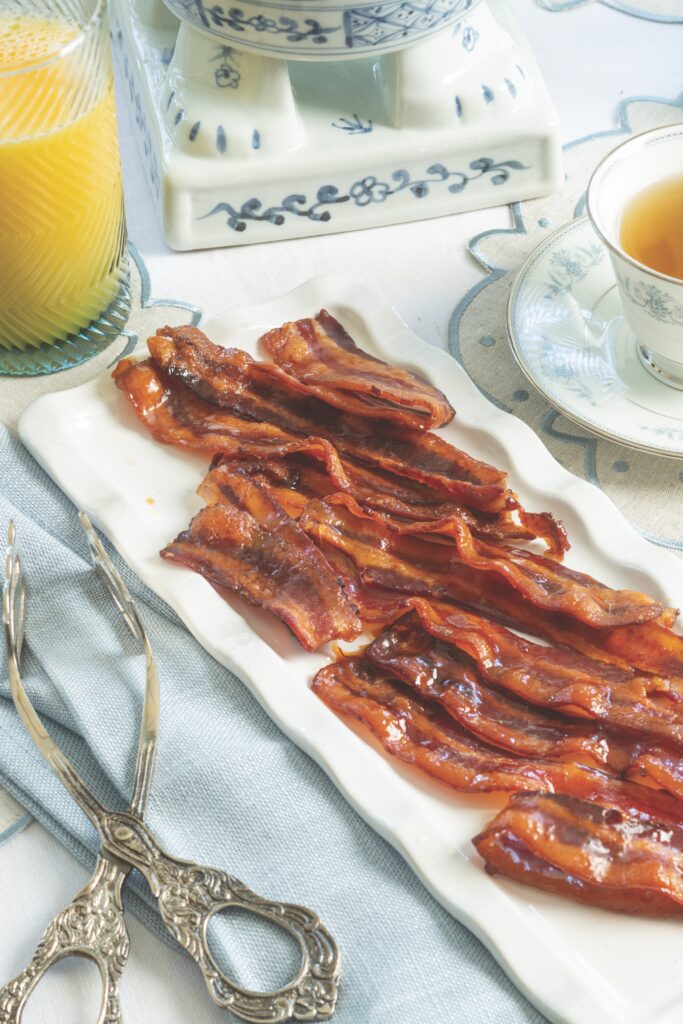 Maple Candied Bacon on a white platter with silver serving tongs.