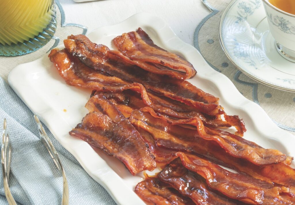 Maple Candied Bacon on a white platter with silver serving tongs.