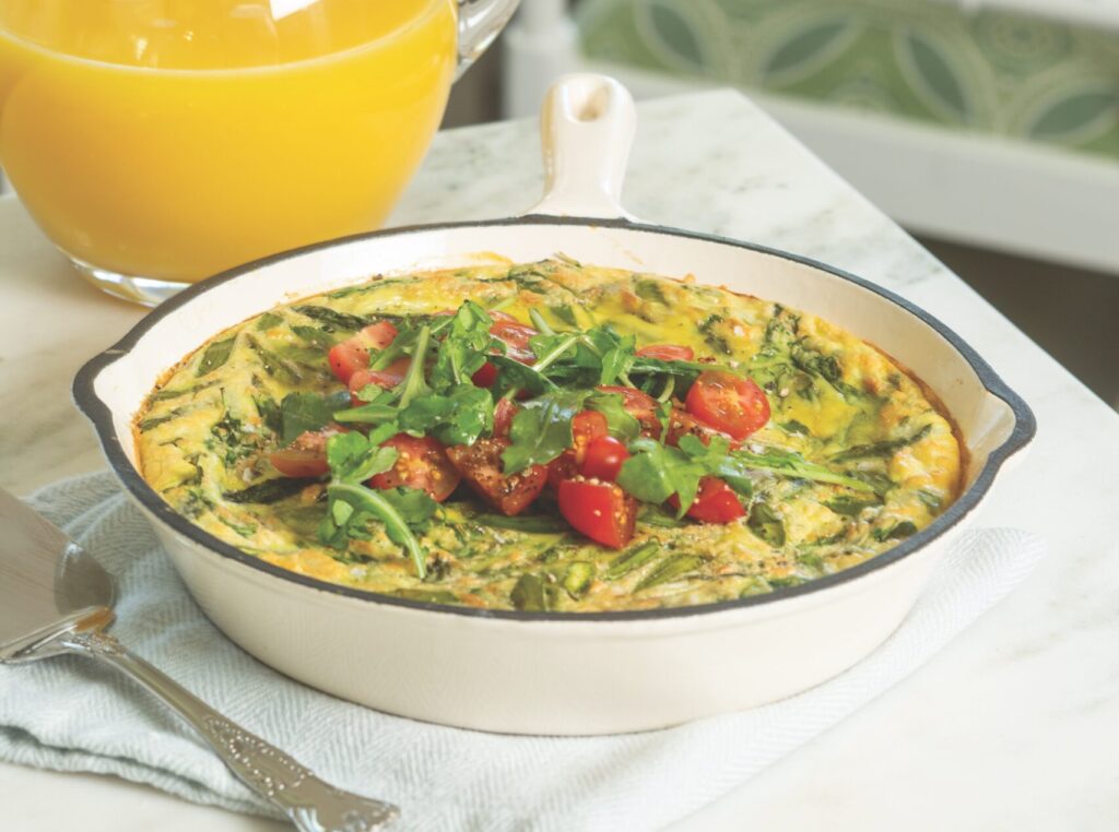 Arugula and Tomato Frittata in a cast iron skillet, with a pitcher of orange juice.