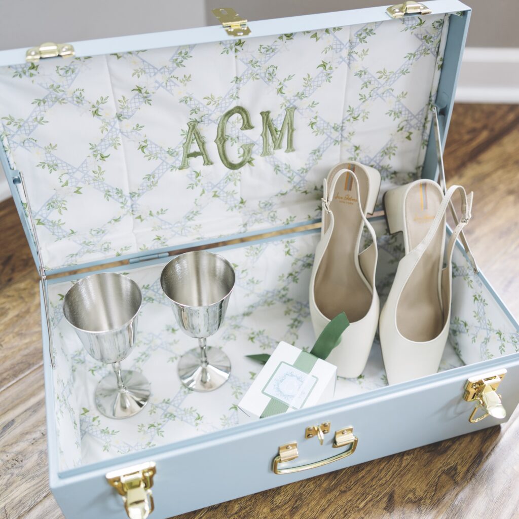A bride's blue keepsake trunk with goblets, high heels, and a gift tag inside.