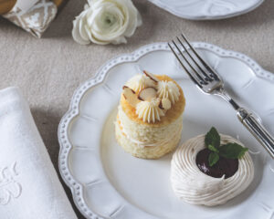 Two small vanilla cupcakes with white swirled frosting and almond slices on a decorative white plate, with a fork nearby.
