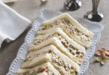 Green Grape–Chicken Salad Tea Sandwiches Triangular sandwiches filled with tuna salad and diced celery on a decorative plate.