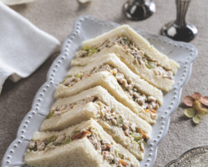 Triangular sandwiches filled with tuna salad and diced celery on a decorative plate.