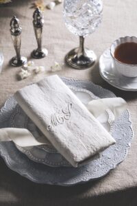 Elegant table setting with stacked decorative plates, a folded linen napkin, and a teacup on the right.