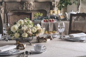 Elegant dining table with a white floral centerpiece, crystal goblets, and a tiered dessert stand of pastries and cupcakes in a refined setting.