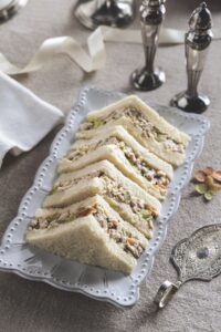 Triangular chicken salad sandwiches arranged on a decorative white platter.