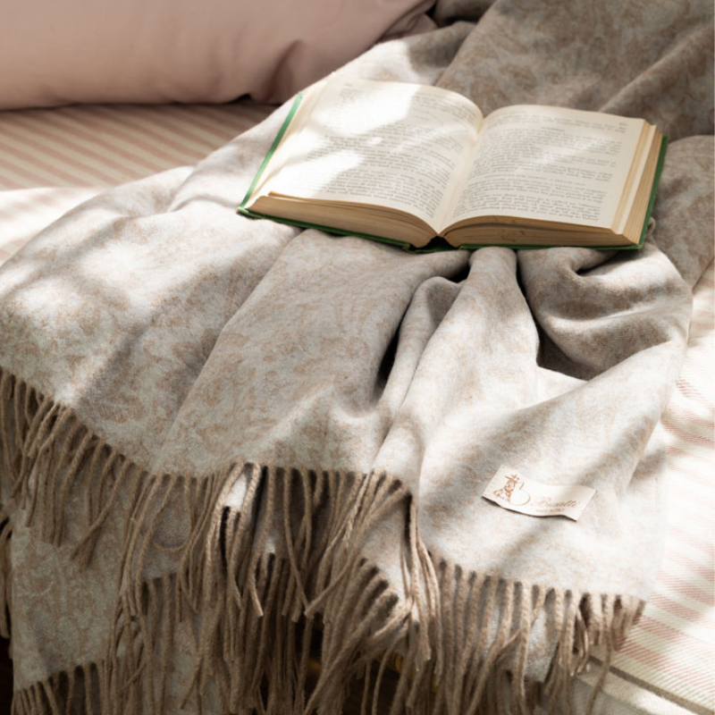 Open book resting on a soft beige throw blanket on a bed, sunlit and cozy.