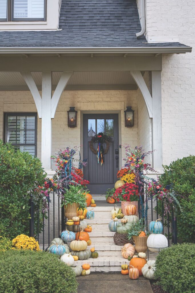 A white brick home with a front walkway lined with heirloom pumpkins and floral arrangements attached to the black iron handrails.