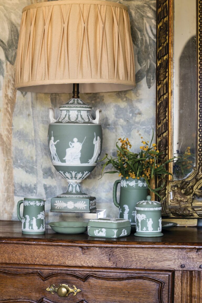 A celadon-green Wedgwood jasperware lamp, lidded boxes, and small vases arranged on a walnut chest beneath a gilt mirror